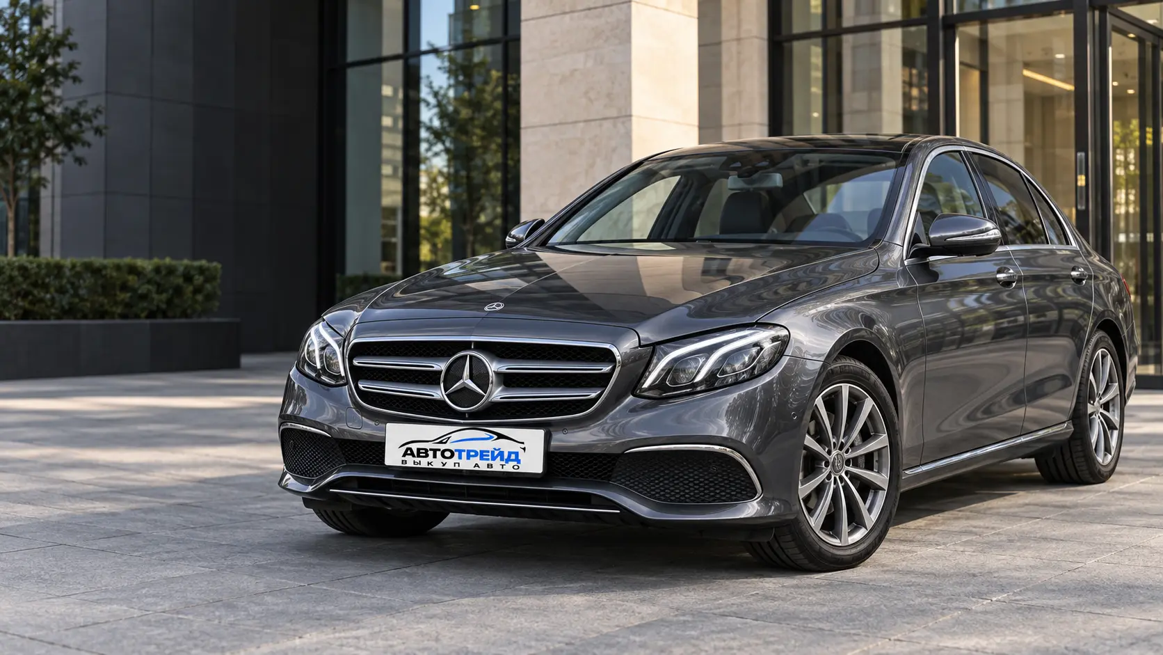Графитовый Mercedes-Benz E-Class на стоянке у современного офисного здания